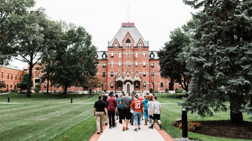 A group of students walking up the lawn toward a brick college hall