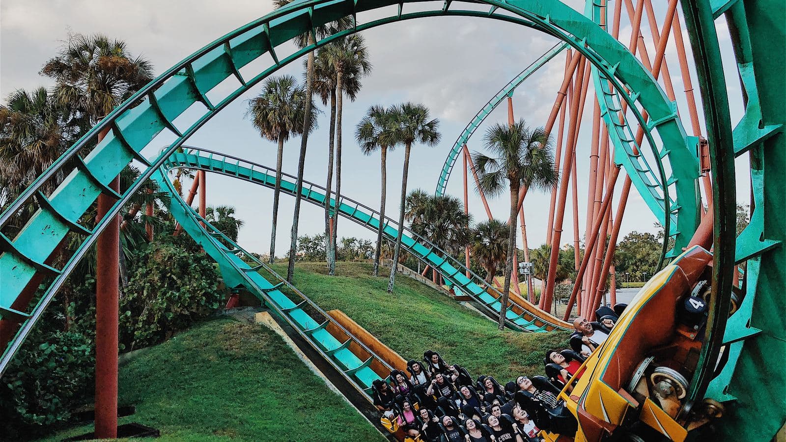 A teal roller coaster looping through palm trees at a theme park