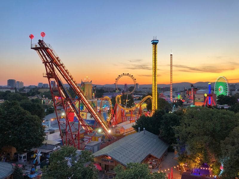 An amusement park with roller coasters and a Ferris wheel lit up at sunset