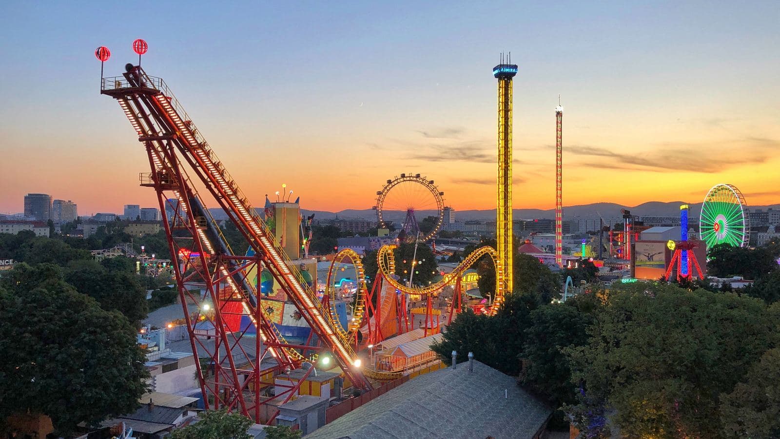 An amusement park with roller coasters and a Ferris wheel lit up at sunset