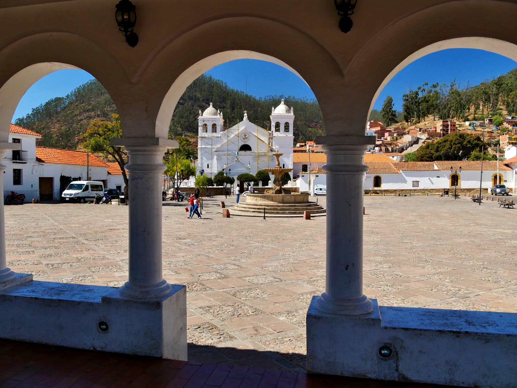 A plaza and white church in Sucre, seen through courtyard arches