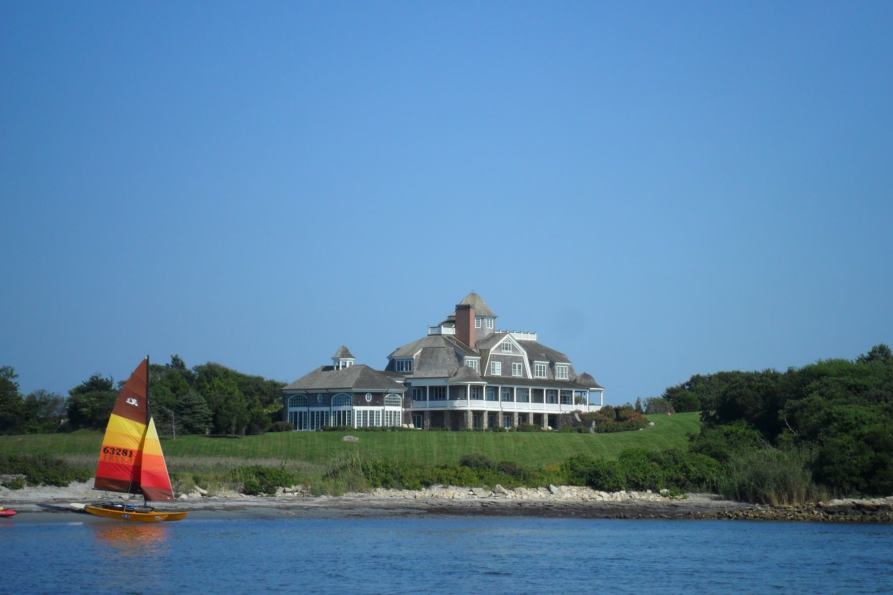 A sailboat on the water in front of a waterfront estate on Ocean Drive in Newport