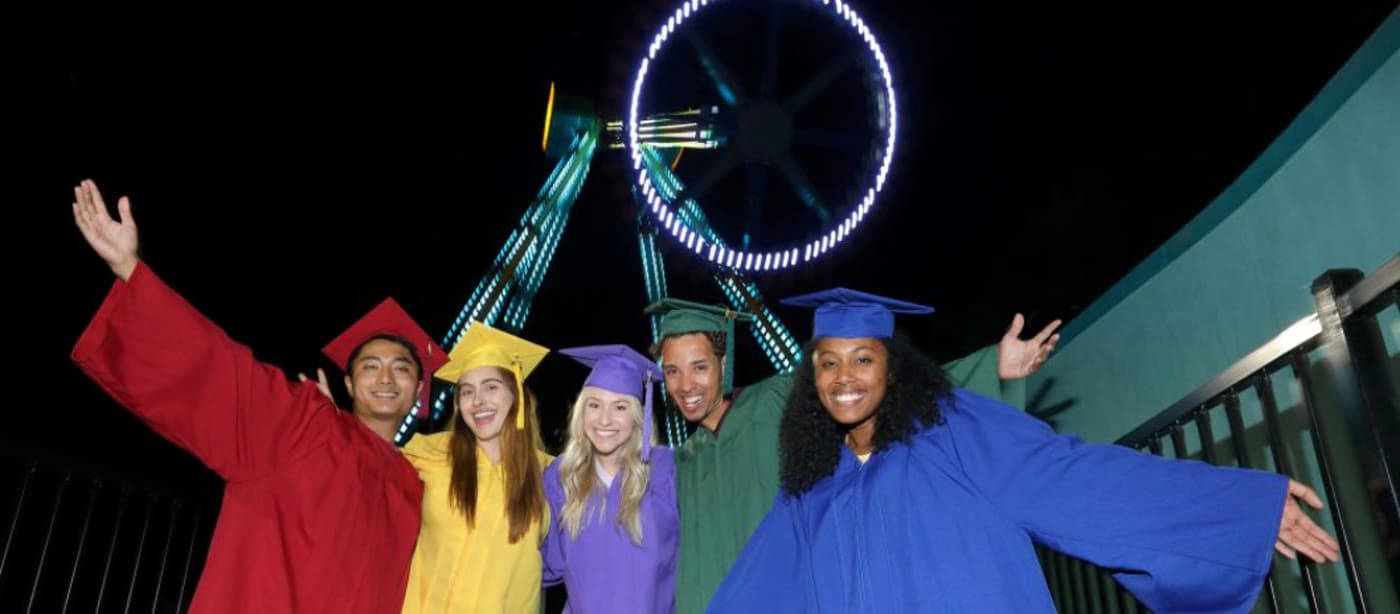 Graduates in caps and gowns in front of a Six Flags ride